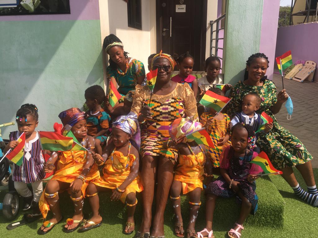 children in african wear sitting on the
                            stairs holding Ghana flags